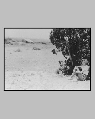 <adrienne posed by a cedar tree. Adron's blacksmith shop can be seen in the background.>