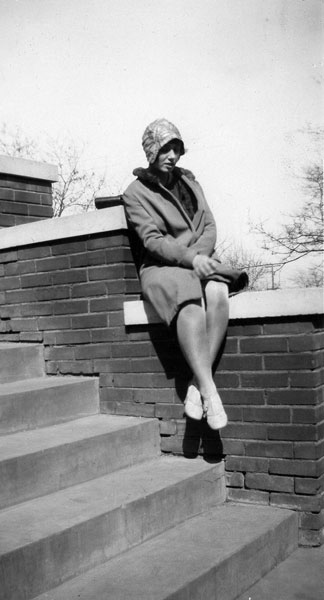 <johnie posed on steps wearng a hat and coat with a fir colar>