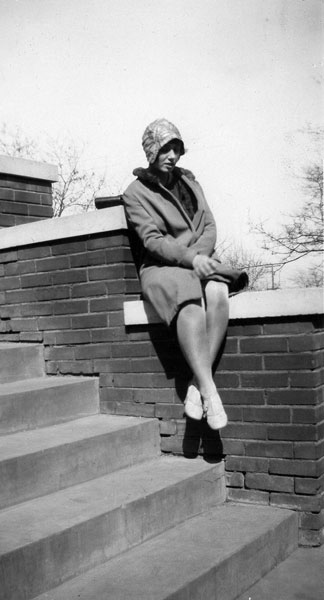 <johnie posed on steps wearng a hat and coat with a fir colar>