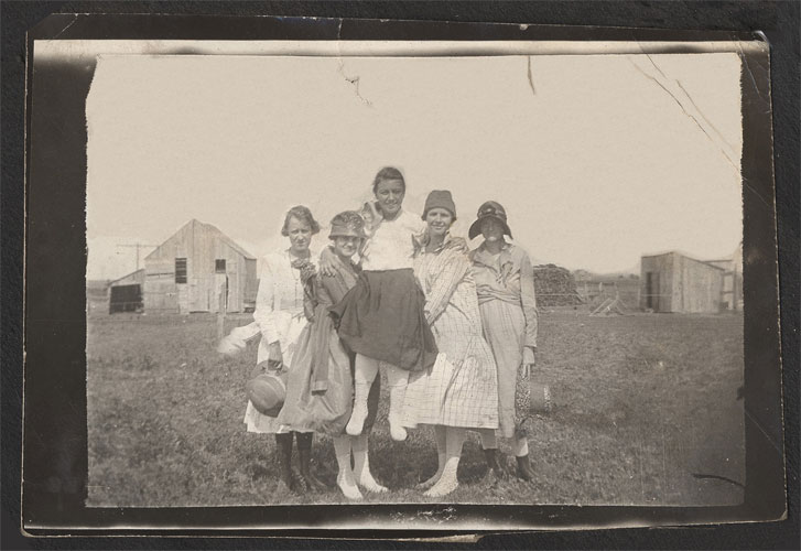 <Five ladies johnie being held up in center. interesting background barns and haystack white stockings>