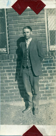 <unknown man posed by brick wall, possibly the school house wall.>