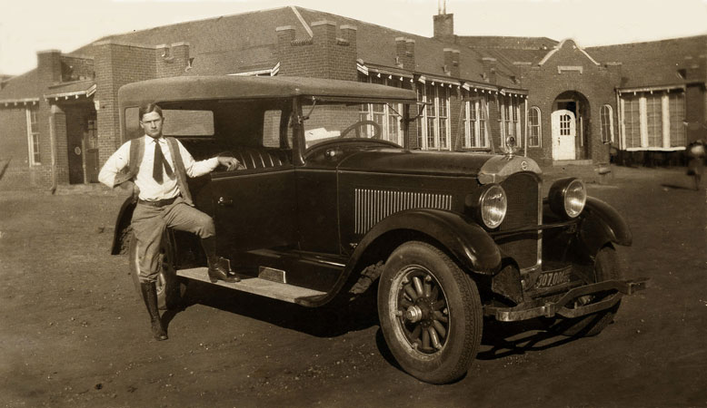<man posed in front of school building with fancy car restored by terry>
