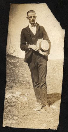<man posed on a windy day holding his straw boater hat in his hand.>