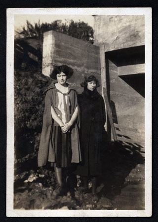 <two ladies posed by a concrete bridge abutment>