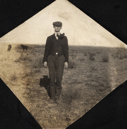 <man standing in a field on a windy day. Horses in the background.>