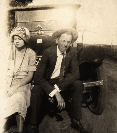 <couple sitting on modle t bumper. The man is wearing a gents straw boater>