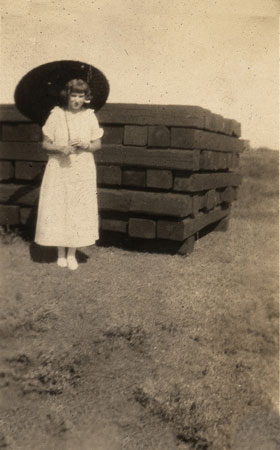 <lady with umbrella standing by stack of cross ties>