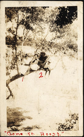 <The photo shows two ladies and a boy sitting on a tree branch, which may be protruding over a body of water. The numbers “1” and “2” are drawn under the ladies. The photo has the caption, “Gone to Roost.”>
