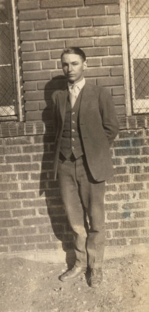 <man wearing suit tie and vest standing by a brick wall probably the wall of the texola school house>